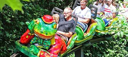 Lachende Familie in Froschbahn die durch den Wald fährt